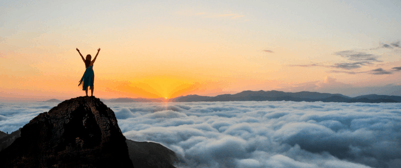 A visionary woman standing atop a mountain at sunrise