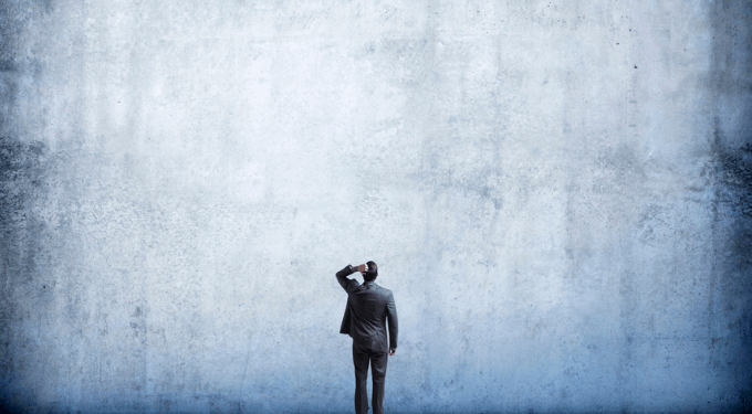 Man staring up at a big blank wall, scratching his head