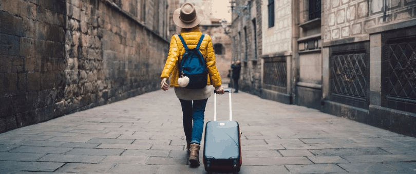 Woman walking down a European cobblestone street pulling a suitcase