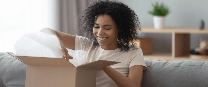 A woman happily digs into a box with bubble wrap, presumably accepting delivery of a luxury item.