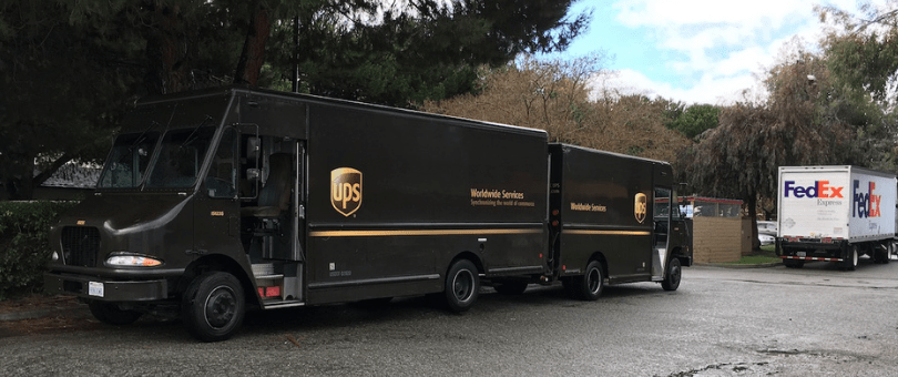 UPS and FedEx trucks parked in a rain-soaked parking lot