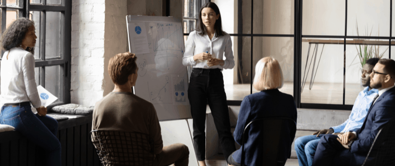 A woman at a whiteboard leading a sales seminar with collagues