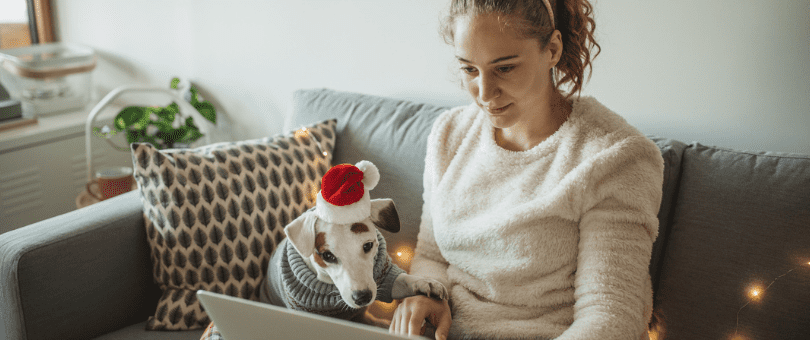 A woman holiday shopping on a laptop with her small dog watching