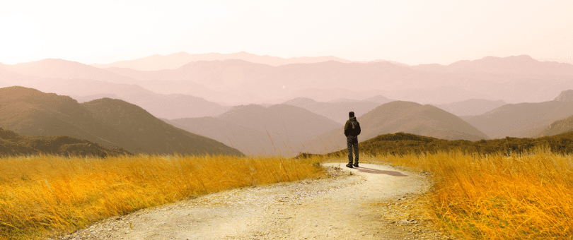 A human figure standing on a winding path out in the country with mountains