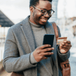 A man standing outside, making an online purchase with his smartphone and credit card
