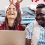 A couple laughing it up sitting on the floor with a laptop, holiday shopping