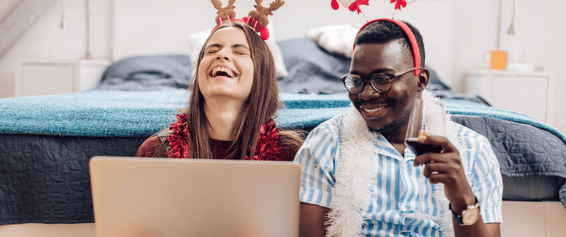 A couple laughing it up sitting on the floor with a laptop, holiday shopping