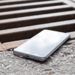 An iPhone sits on the precipice of a storm drain