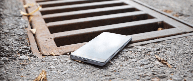 An iPhone sits on the precipice of a storm drain