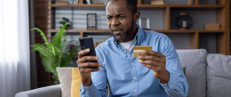 A man, frustrated, with mobile phone and credit card in his hand to illustrate Signifyd false declines blog