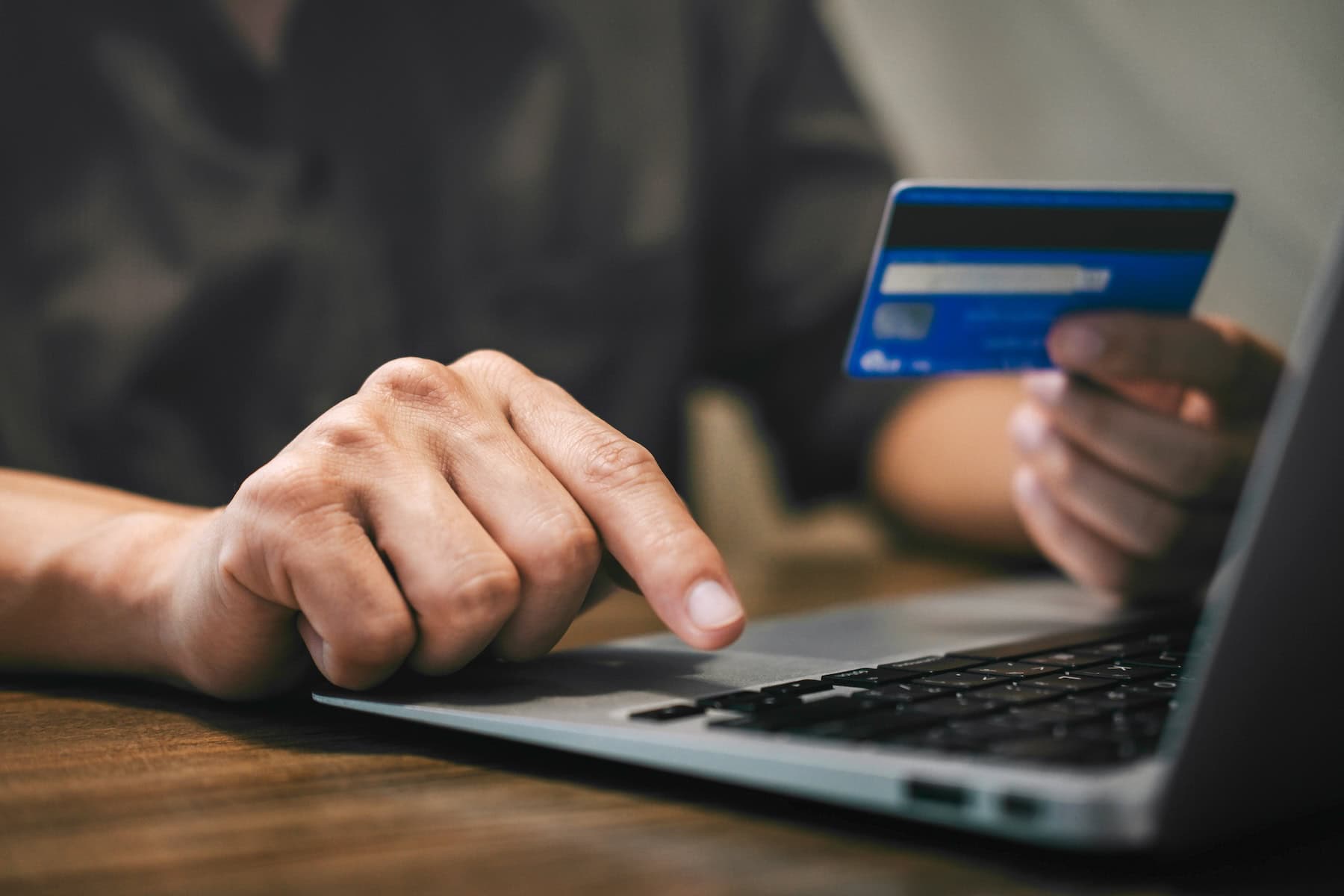 a hand typing on a laptop with another hand holding a credit card -- shopping online