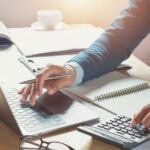 A man sitting at a laptop with calculator to illustrate new fees for Stripe and Visa concerning chargeback disputes