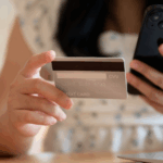Woman holding a credit card, a mobile phone, sitting by a laptop to illustrate payment optimization