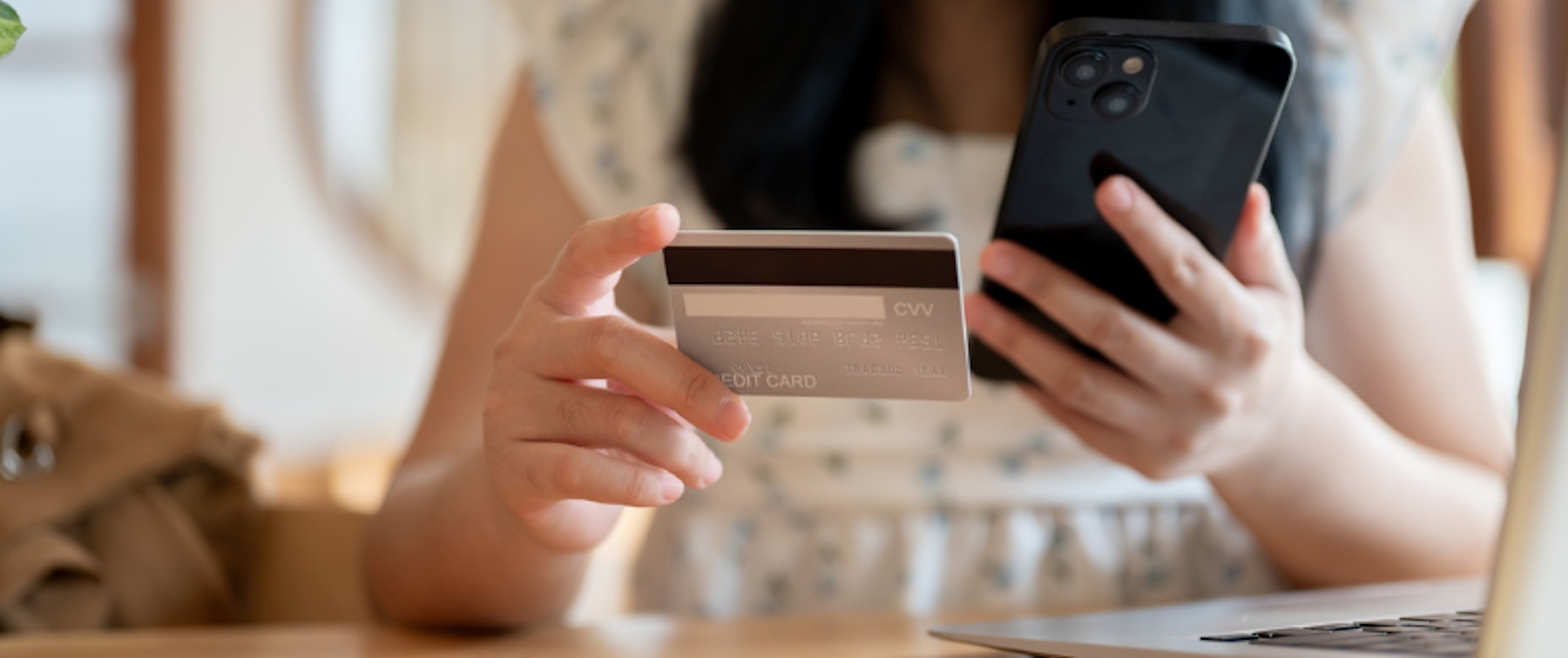 Woman holding a credit card, a mobile phone, sitting by a laptop to illustrate payment optimization
