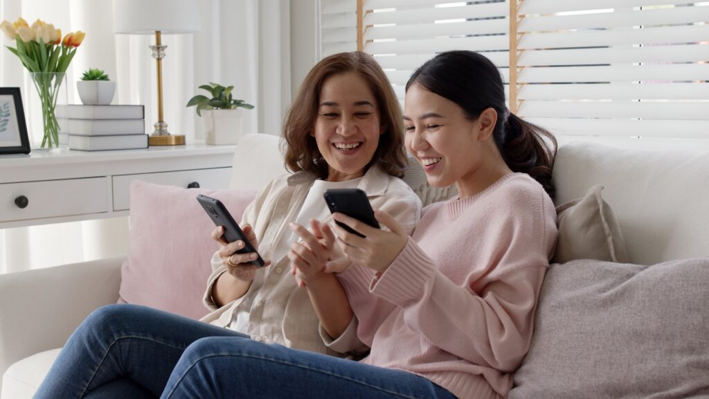 Two friends on a couch, beaming and laughing while buying online