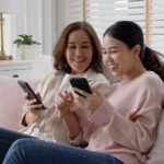 Two friends on a couch, beaming and laughing while buying online