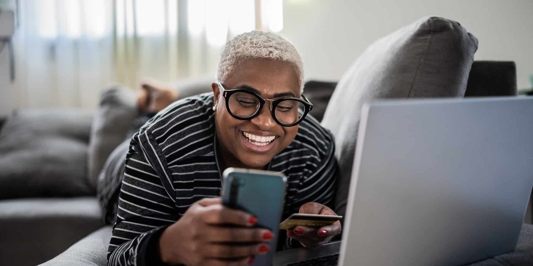A smiling woman shopping online while laying on a couch