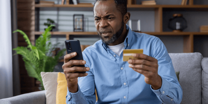A man, frustrated, with mobile phone and credit card in his hand to illustrate Signifyd false declines blog