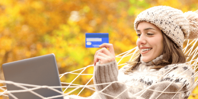 A woman in stocking cap and cozy sweater relaxed and shopping online in a hammock