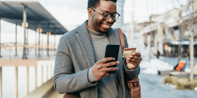A man standing outside, making an online purchase with his smartphone and credit card