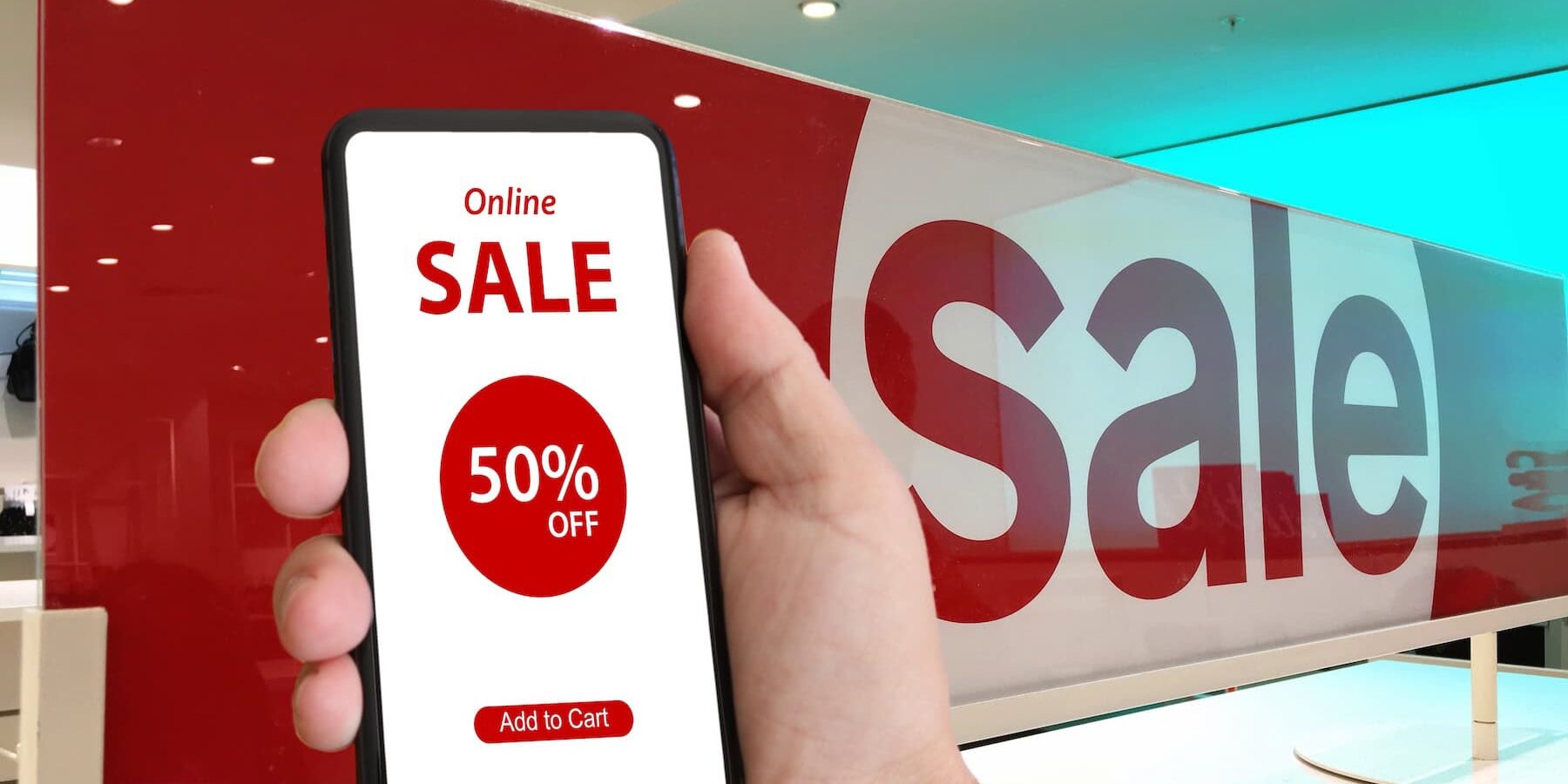 shopper with a mobile device displaying 50% off sale in forefront of big "Sale" sign.